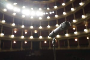 Close-up of a microphone on stage with bright theater lights in the background.